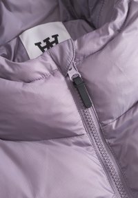 Interior de chaqueta acolchada de color púrpura claro con una textura suave, que cuenta con una cremallera YKK y una etiqueta con un logo negro en el cuello.