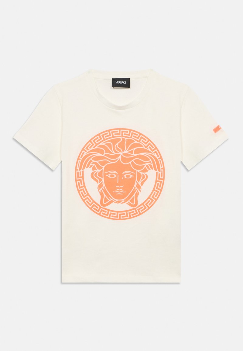 Μπεζ βαμβακερό μπλουζάκι με πορτοκαλί γραφικό Medusa και περίγραμμα με ελληνικό κλειδί. Κοντά μανίκια, στρογγυλή λαιμόκοψη και ετικέτα Versace στο γιακά.