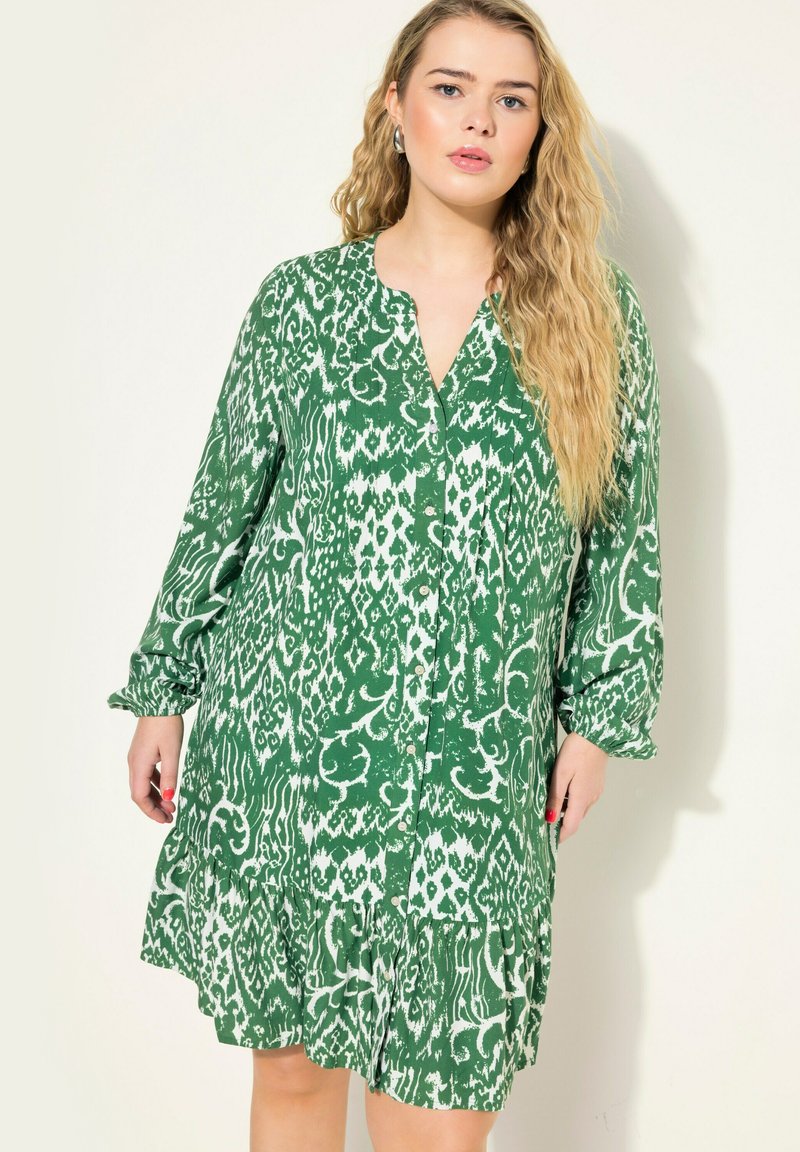 Robe verte à motif en tissu léger, avec un décolleté en V, des manches longues avec des poignets froncés, et un ourlet à volants.