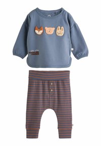 Felpa azzurra chiara con applicazioni di animali (volpe, orso, coniglio) e testo "Piccole Creature del Bosco Carine", abbinata a pantaloni a righe marroni.