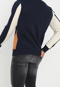 Felpa pullover navy con pannelli laterali color crema e arancio, polsini e orlo a costine, realizzata in un morbido tessuto testurizzato.