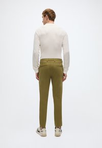 Ανοιχτό μπεζ μακρυμάνικο τοπ, παντελόνι σε ελαιί πράσινο με στενή γραμμή, και κρεμ αθλητικά παπούτσια με μαύρες λεπτομέρειες. Ομαλή υφή, εφαρμοστό σχέδιο με πίσω τσέπες.