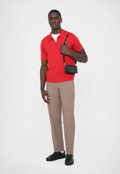 Punainen teksturoiduilla yksityiskohdilla varustettu lyhythihainen poolopaita, ruskeat räätälöidyt housut ja mustat lenkkarit; musta olkalaukku, jossa kullanväriset kirjaimet.