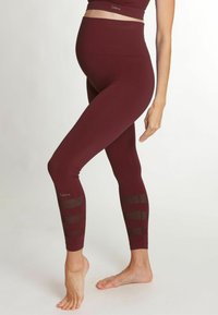 Leggings de maternité en bordeaux foncé, présentant une texture lisse, une taille haute et des accents rayés translucides au bas des jambes.
