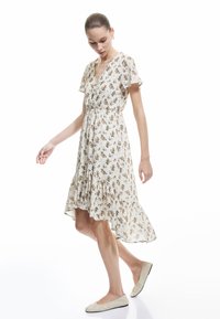 Vestido floral con escote en V, mangas cortas con volantes y un dobladillo en capas. Tejido ligero con un fondo crema y pequeñas flores multicolores.