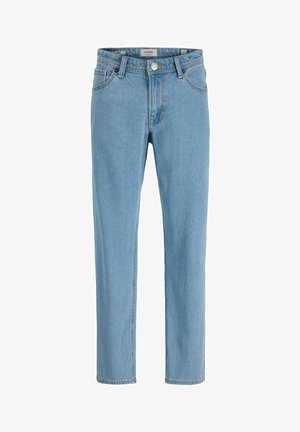 Garçon souriant qui se tient face à l'avant, portant une chemise blanche à manches longues, un jean bleu clair et des baskets blanches sur un fond uni.