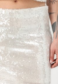 Gonna decorata con paillettes in beige chiaro con righe verticali, caratterizzata da una superficie liscia e un luccichio contrastante grazie a numerose piccole paillettes.