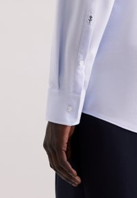 Camicia da uomo in twill azzurro chiaro con maniche a polsino abbottonato e ricamo floreale nero. Tessuto liscio e vestibilità su misura.