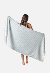Manta ligera de algodón en un patrón de cuadros azul y crema, con bordes con flecos. Colgada sobre un hombro, presenta un tejido texturizado.