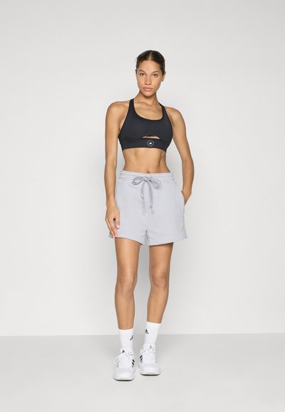 Μαύρο σπορ σουτιέν με λεπτομέρεια κοπής, συνδυασμένο με ανοιχτό γκρι σορτς με ελαστική μέση και κορδόνι, φόρεμα με λευκά παπούτσια.