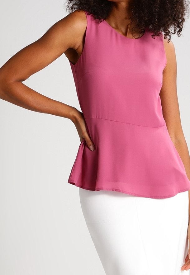 Haut style peplum en tissu rose à texture lisse. Design sans manches avec un col rond et un ourlet évasé, porté avec une jupe blanche.