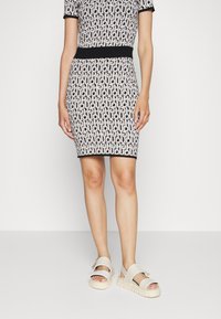 Bodycon jurk met een zwart-wit geometrisch patroon, korte mouwen en een zwarte tailleband; gecombineerd met chunky, strap-sandalen.