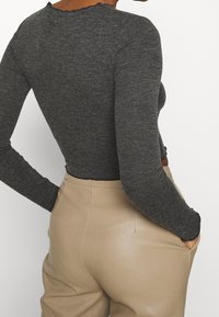 Szara prążkowana bluzka z długim rękawem z surowym wykończeniem na brzegu, zestawiona z beżowymi dopasowanymi spodniami, podkreślająca fakturę i przylegający krój.