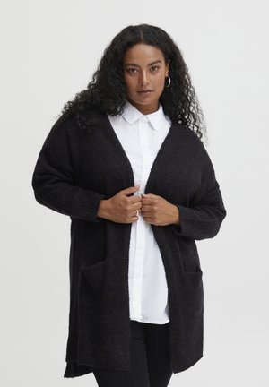 Dark wool cardigan with an open front, two front pockets, and long sleeves, worn over a white collared shirt. Textured fabric, loose fit.