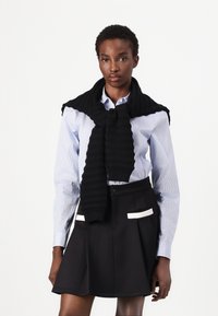 Scarf nera a coste appoggiata su una camicia a strisce blu chiaro, abbinata a una gonna nera plissettata con dettagli in bianco sulle tasche.