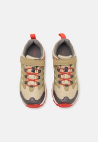 Zapatillas deportivas beige con parte superior de malla, detalles grises, cordones rojos y una correa de Velcro. Presenta una suela texturizada para mayor agarre. Dos lengüetas.