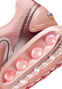 Zapatilla deportiva rosa con una parte superior texturizada y un acabado liso, burbujas de amortiguación de aire visibles y una suela con diseño.