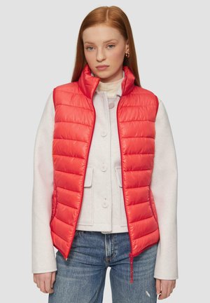 Red padded vest with a zipped front, featuring a high collar, styled over a light gray sweater and blue jeans. Smooth texture and quilted design.