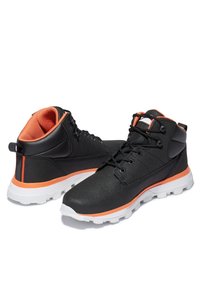 Des chaussures montantes noires avec des accents orange, en tissu texturé, dotées d'œillets renforcés et d'une semelle en caoutchouc blanc avec un motif de semelle robuste.