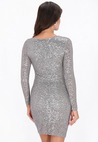 Glänzendes silbernes Minikleid mit langen Ärmeln, bedeckt mit Pailletten. Eng anliegendes Design mit rundem Ausschnitt, das eine glatte, strukturierte Oberfläche hervorhebt.