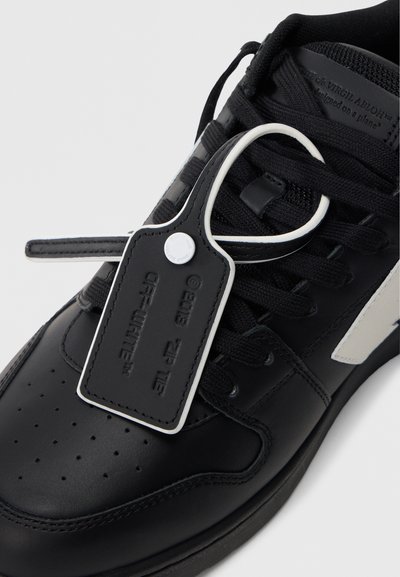 Μαύρο δερμάτινο αθλητικό παπούτσι με λευκές λεπτομέρειες, διαθέτοντας διάτρητη μύτη, μαύρα κορδόνια και προσαρτημένη ετικέτα με φερμουάρ που αναγράφει «OFF-WHITE».