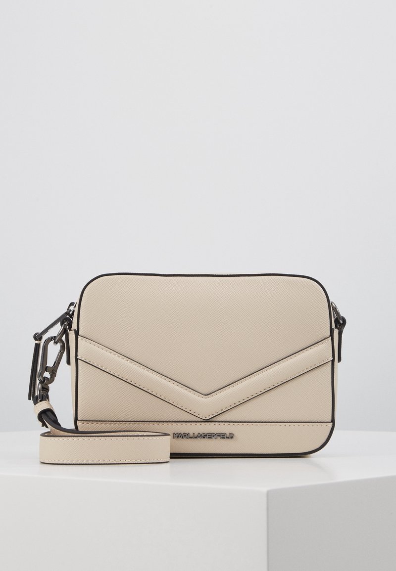 Beżowa torebka na ramię o fakturowanej powierzchni, z wzorem w jodełkę, czarną lamówką i odpinanym paskiem. Logo tłoczone z przodu.