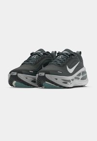 Nike løpesko med overdel i mørkegrå netting, lys grå midtsåle, teksturert såle og hvite detaljer, med intrikate designlinjer og lisser.