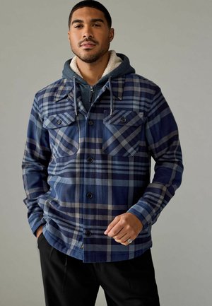 Navy and blue checkered flannel jacket with two chest pockets, button closure, and a gray hooded sweatshirt layered underneath.