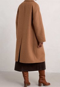 Brown wool coat with a loose fit, drop shoulders, and a center back seam, paired with a dark brown corduroy skirt and knee-high boots.