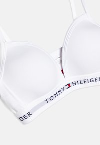 Soutien-gorge blanc rembourré en tissu lisse avec des bretelles réglables. Présente une taille logo saillante affichant "TOMMY HILFIGER" en lettres grasses.