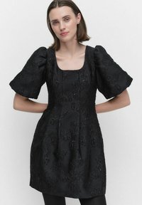 Svart klänning med puffärmar, fyrkantig urringning, texturerat tyg med blommönster och en figursydd bodice som vidgar sig vid midjan.