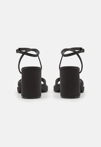 Černé sandály na podpatku s blokovým podpatkem, s elegantním designem pásků a uzávěrem kolem kotníku. Hladký povrch s minimalistickým stylem.