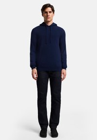 Marinblå huvtröja i strukturerad tyg med dragsko, långa ärmar och en avslappnad passform, kombinerad med mörk denimjeans och svarta skor.