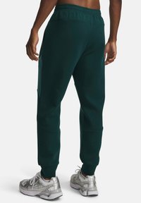 Grüne Baumwoll-Jogginghose mit elastischem Bund, Seitentaschen und zulaufenden Beinen, kombiniert mit silbernen Sportschuhen.