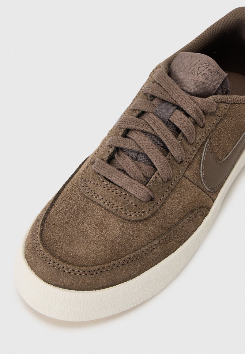 Zapatillas de ante marrón con punta redondeada, cordones a tono y una suela de goma blanca. Presenta un logo sutil en el lateral y una parte superior texturizada.