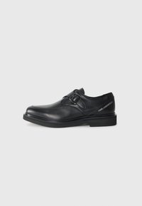 Black leather shoe with a rounded toe, single buckle detail, and flat rubber sole. Features branding on the side near the heel.