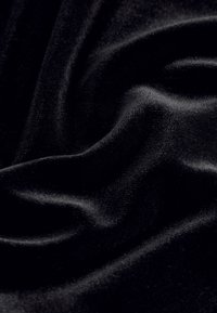 Tissu en velours noir avec une texture lisse et un éclat réfléchissant, présentant des plis doux et des ondulations subtiles.