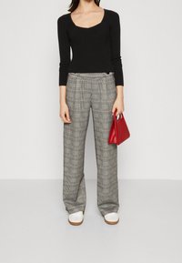 Svart ribbad långärmad topp, grå rutig vida byxor och en röd handväska. Skorna är vita med en tan sula.