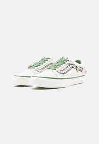 Baskets en toile avec une tige blanche, des accents verts, des coutures détaillées et des breloques décoratives sur les lacets. Semelle en caoutchouc, bout arrondi.
