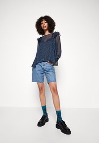 Top azul marino transparente con acentos de volantes y estampado, combinado con pantalones cortos de mezclilla claros y zapatos de plataforma negros. Calcetines estampados en azul y amarillo.