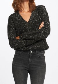 Black, glittery V-neck sweater with ribbed texture, featuring long sleeves. Worn with high-waisted dark jeans, showcasing a fitted silhouette.