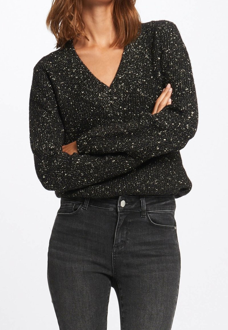 Black, glittery V-neck sweater with ribbed texture, featuring long sleeves. Worn with high-waisted dark jeans, showcasing a fitted silhouette.