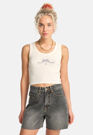 Top corto crema a coste con logo "BILLA BONG" e palma in blu, abbinato a shorts di jeans neri a vita alta con orlo sfilacciato.