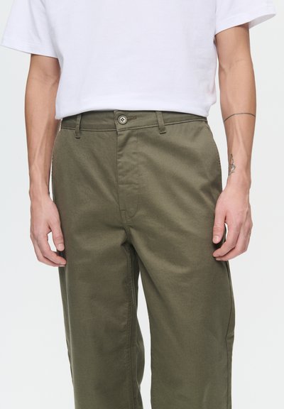 Pantalons en coton vert olive avec une coupe droite, dotés d'une fermeture à bouton à l'avant et de poches latérales. Texture lisse, détails de coutures minimaux.