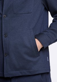 Giacca blu navy realizzata in tessuto texturizzato con chiusura a bottoni, taschino sul petto e tasca laterale nascosta.