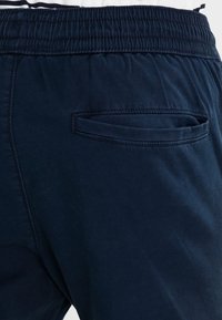 Navy blue elastic waistband trousers with a smooth texture, featuring a single rear pocket with a stitched edge.