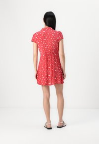 Rochie scurtă roșie cu mâneci scurte, imprimeu floral, talie ajustată, țesătură texturată și fustă evazată. Include un guler și slituri laterale.