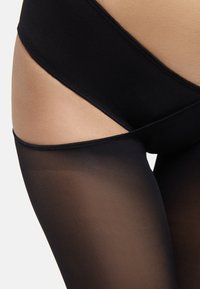 Collant neri opachi con una texture matte, caratterizzati da un design a vita alta e una sezione delle gambe trasparente, che passa da solido a trasparente.