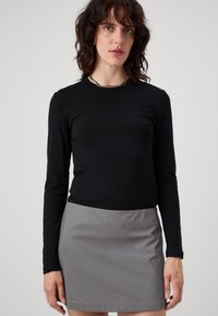 Top nero a maniche lunghe abbinato a una mini gonna grigia. Il top presenta un design aderente, mentre la gonna ha una finitura lucida e un orlo semplice.