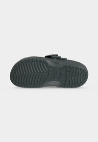 Μαύρο σανδάλι Crocs από την πλευρά της σόλας, με υφή στην επιφάνεια πρόσφυσης και ρυθμιζόμενο λουράκι σε απλό φόντο.
